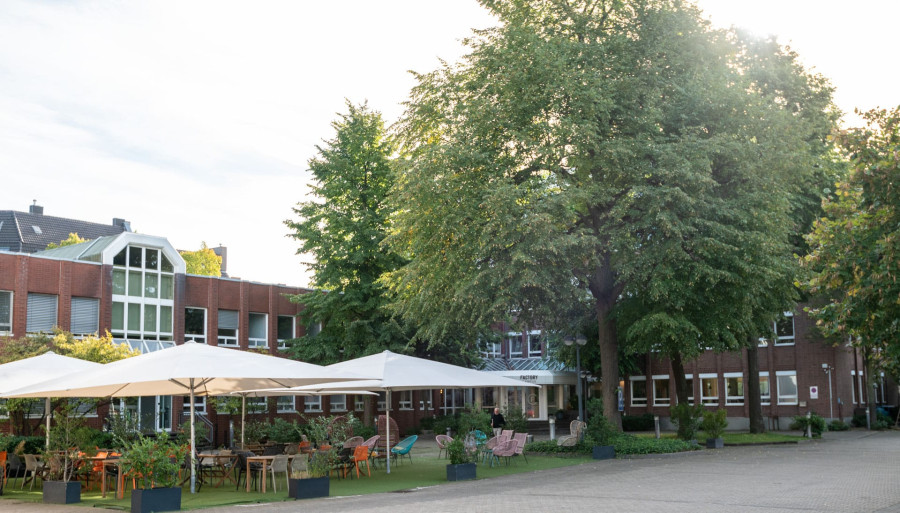 Outdoorbereich des Pioniergeb&auml;udes des Factory Campus, Gr&uuml;nf&auml;che mit Sonnenschirmen