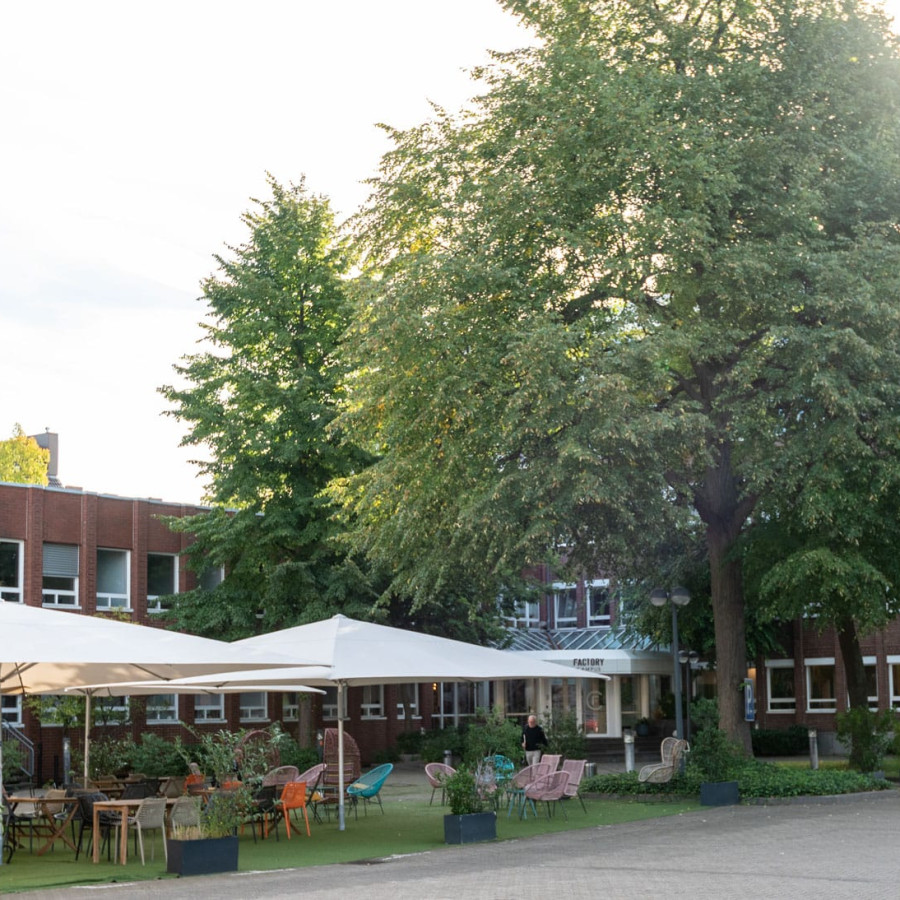 Outdoorbereich des Pioniergeb&auml;udes des Factory Campus, Gr&uuml;nf&auml;che mit Sonnenschirmen