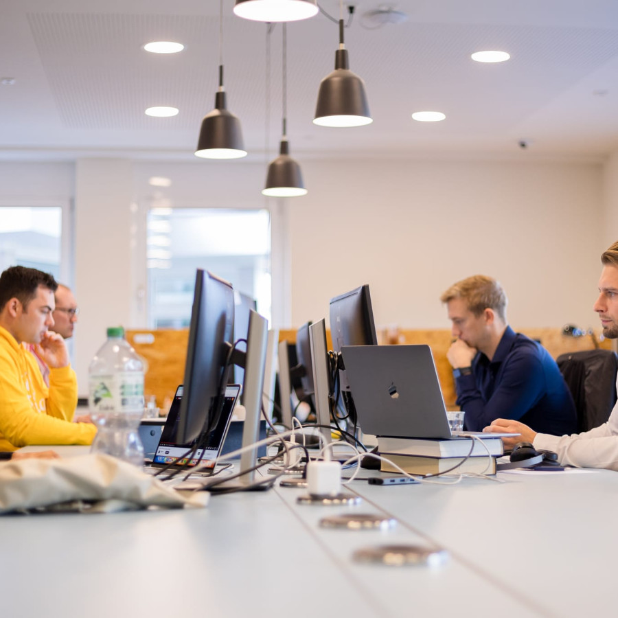 Gro&szlig;er Tisch im Coworking Space, an dem f&uuml;nf Menschen an ihren Computern arbeiten