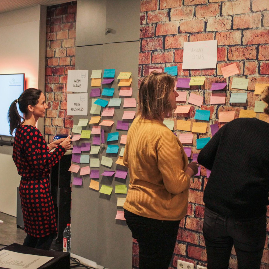 Personen arbeiten bei einem Workshop mit Post-Its an einer Wand