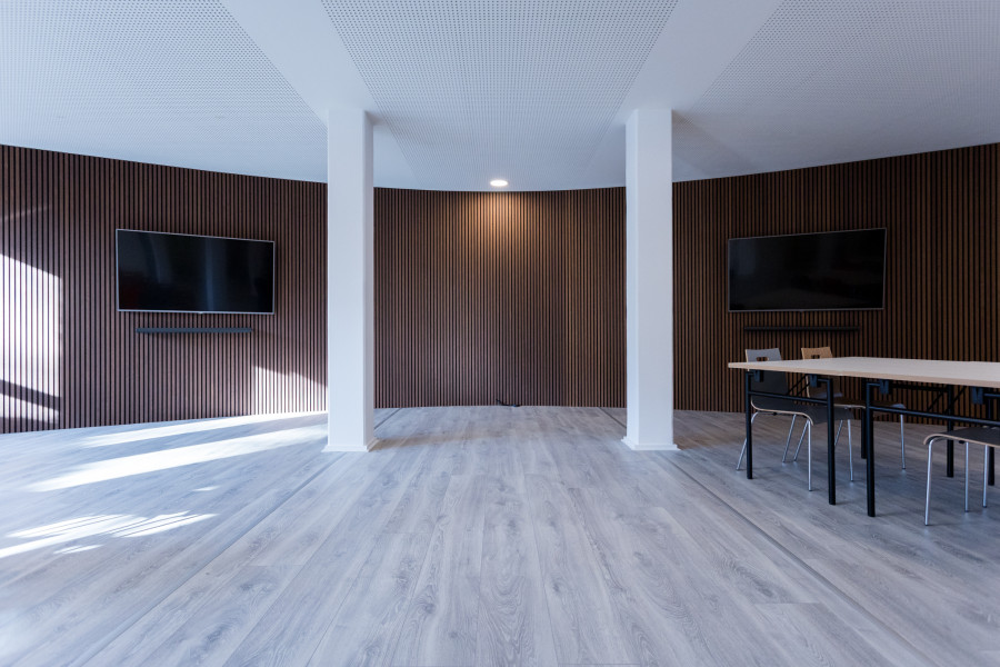 Meetup-Projektraum mit gro&szlig;en Bildschirmen an abgerundeten W&auml;nden mit braunen Paneelen