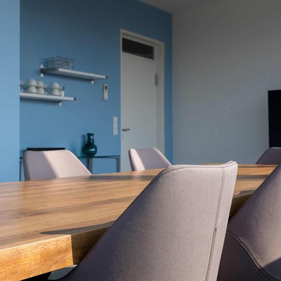 Cloud Konferenzraum mit einem gro&szlig;en Holztisch, hellen St&uuml;hlen und einer auffallenden blauen Wand