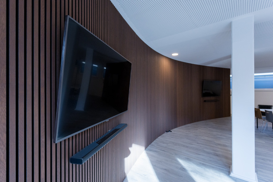 Meetup-Projektraum mit gro&szlig;en Bildschirmen an abgerundeten W&auml;nden mit braunen Paneelen